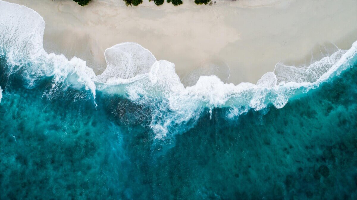 aerial view of wave meeting the beach at the shoreline